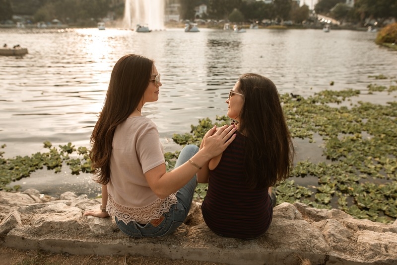 Employee Support and Connection for Workplace Wellbeing Two women sitting by a lake talking and supporting each other, representing employee mental health resources and peer support.