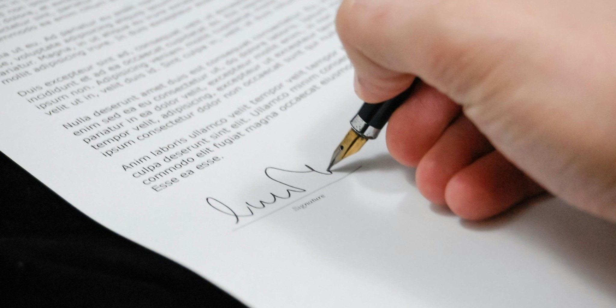Employee signing workplace wellness agreement document Close-up of a person signing a document with a fountain pen, representing employee program participation or workplace wellness agreement.