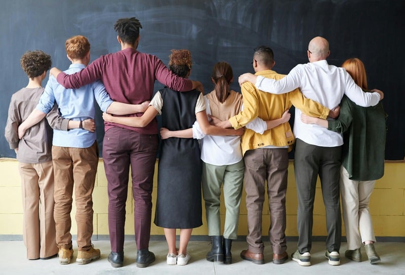 Workplace Team Building and Employee Wellness Support Group of coworkers standing together with arms around each other, representing teamwork and employee wellness in workplace workshops.